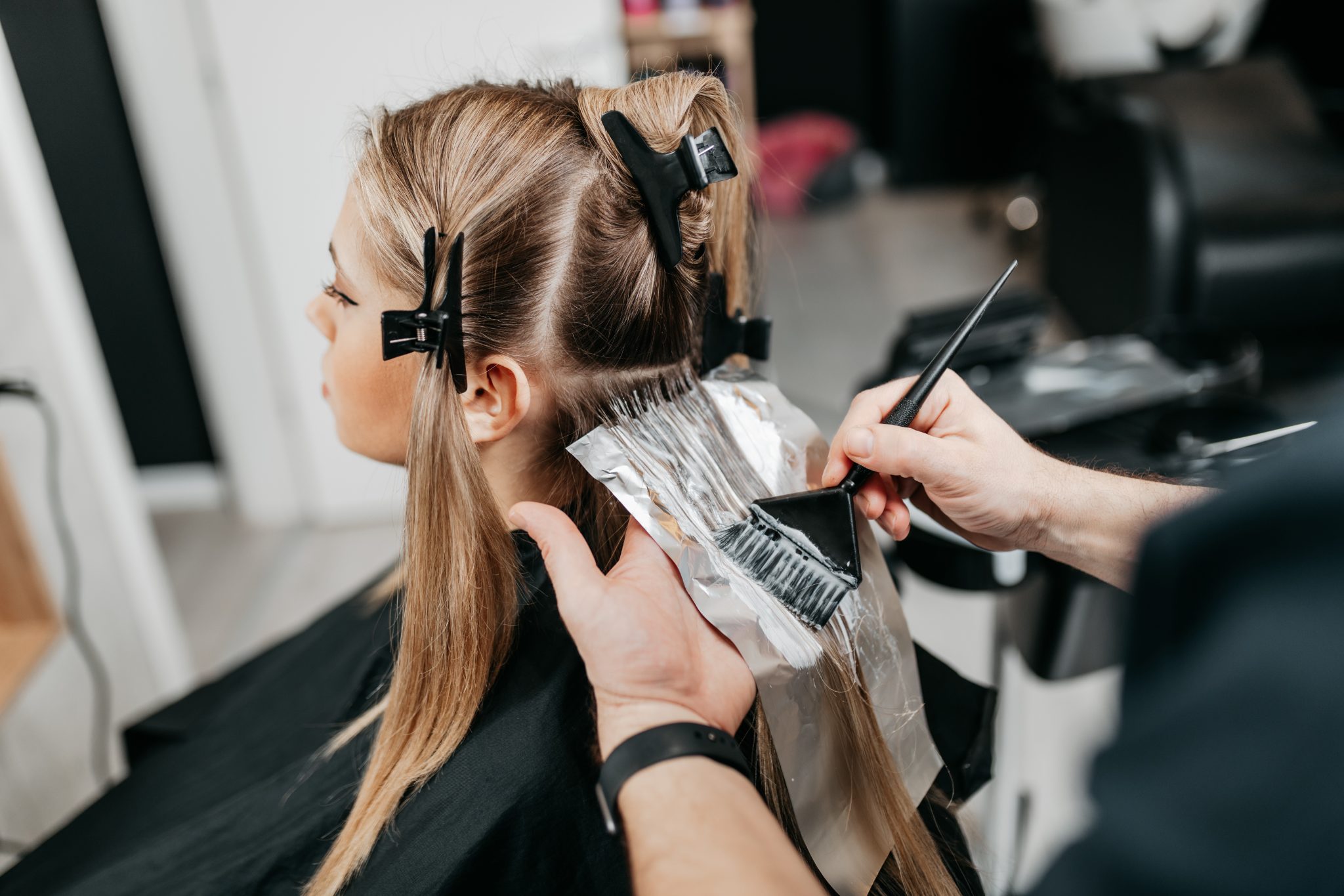 Professional hairstylist applying hair color treatment to young girl's hair in salon