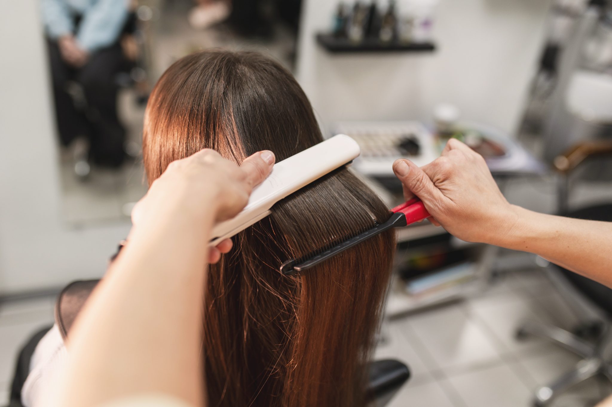 Professional hairdresser applying color treatment to client's long brown hair in salon