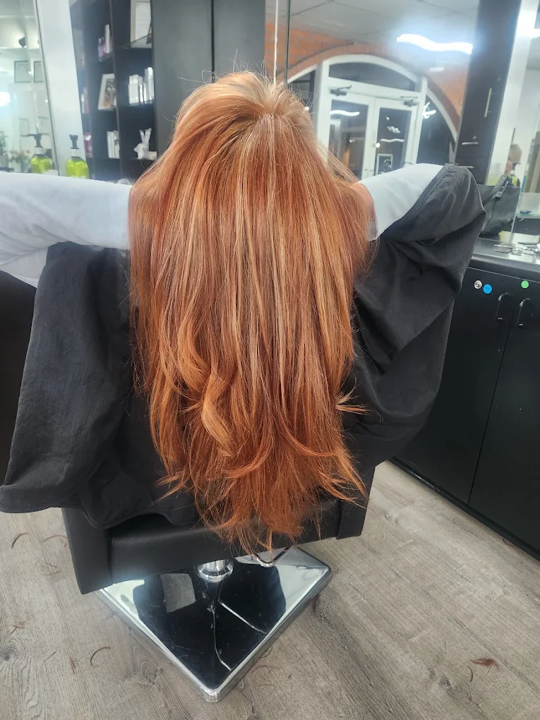 Person with long copper-red hair seated in black salon chair at styling station