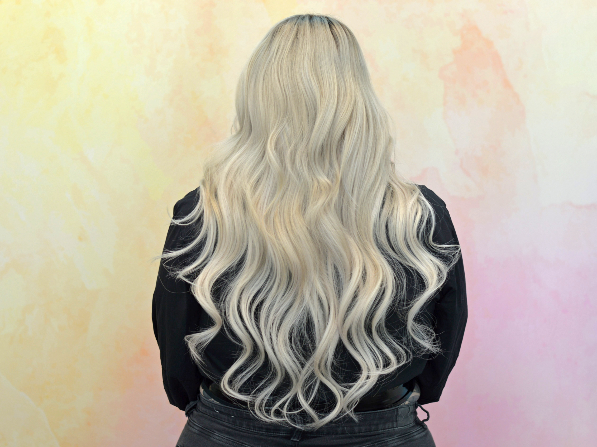 Woman with long silver wavy hair wearing black top, back view against pastel gradient background
