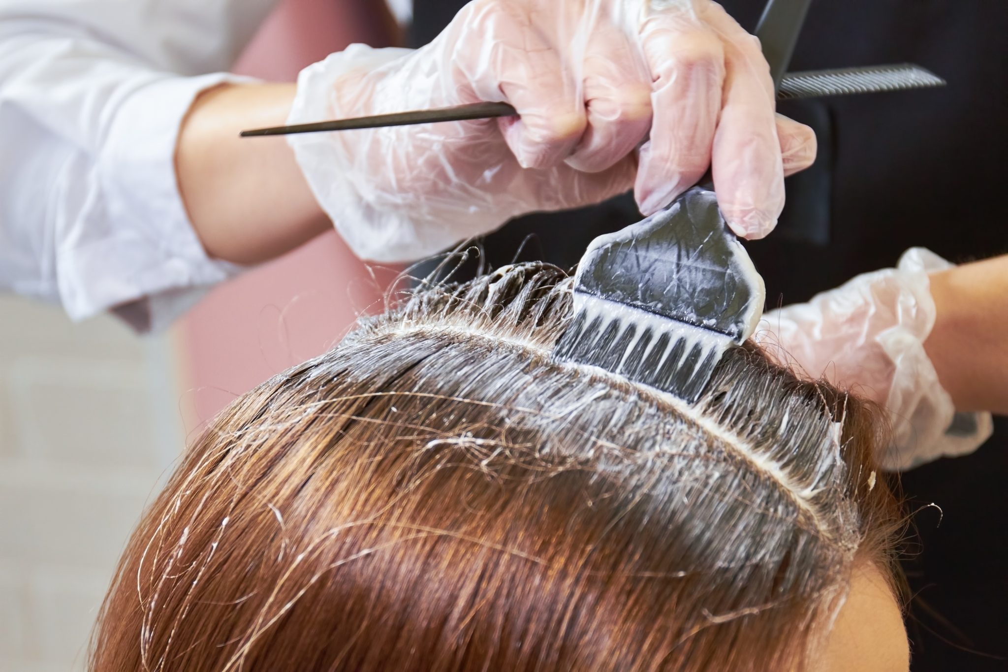 Hair colorist applying dark dye to brown hair with brush and comb wearing plastic gloves