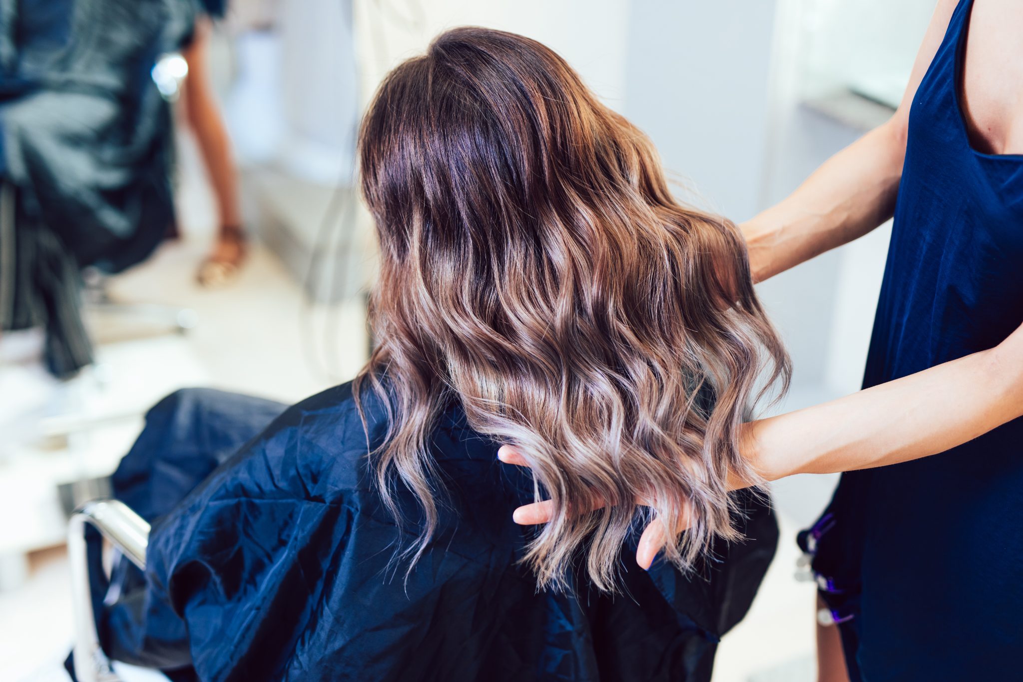 Hairstylist examining client's long wavy brunette hair in salon