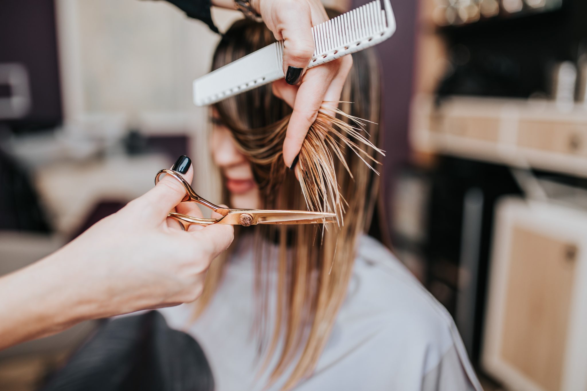Professional hairdresser cutting client's brown hair with scissors and comb in salon