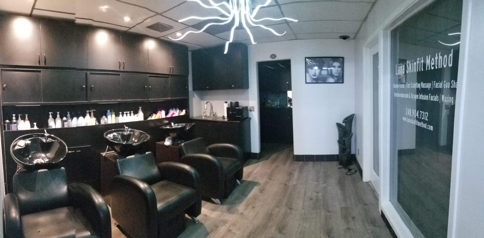 Modern salon interior with black vanity stations, green leather chairs, and neon light fixture
