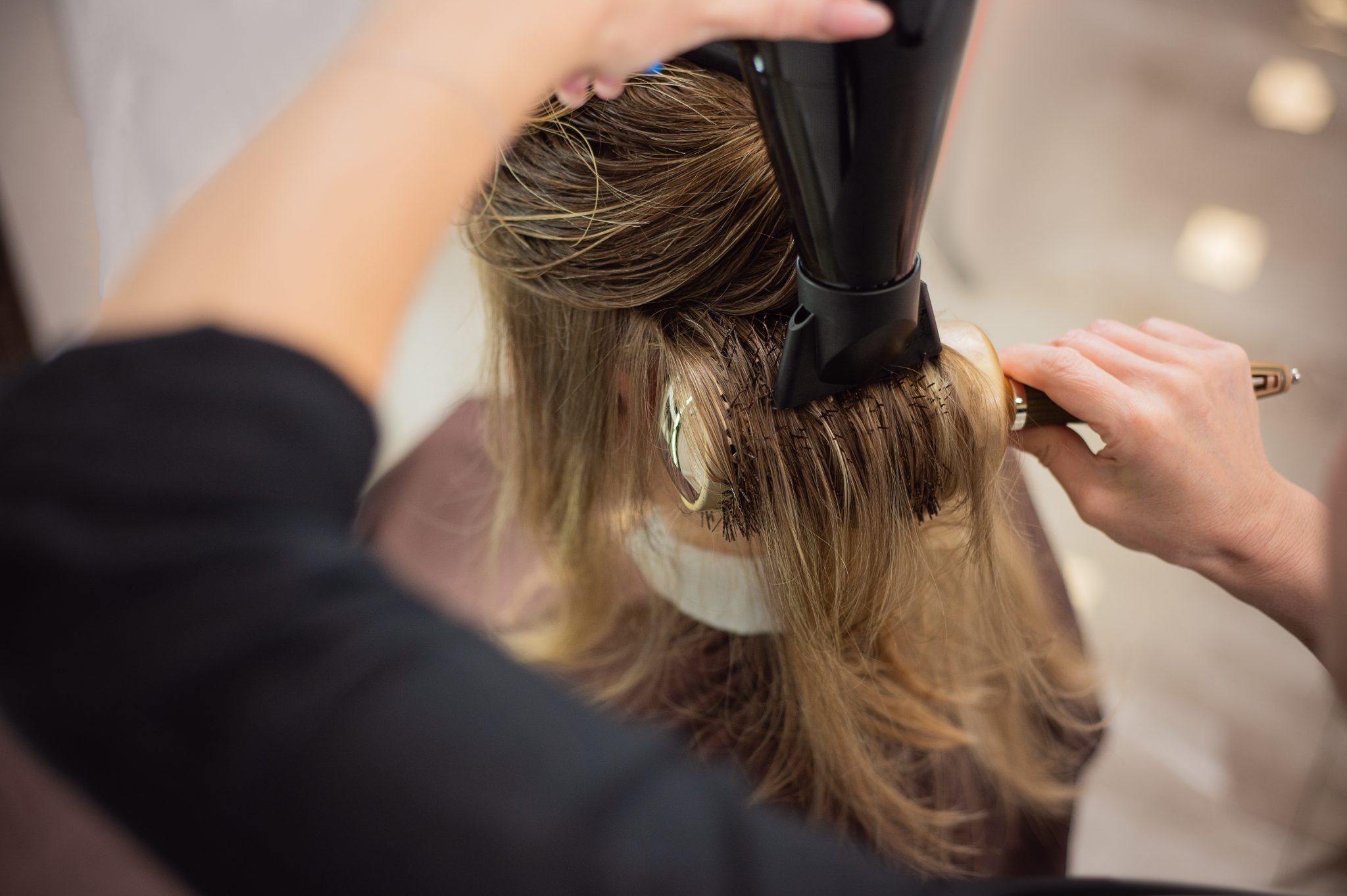 Hairstylist curling long brown hair with a black curling iron