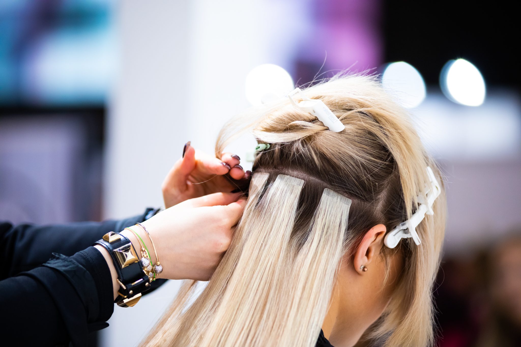 Hairstylist applying hair extensions to client with blonde hair using white clips